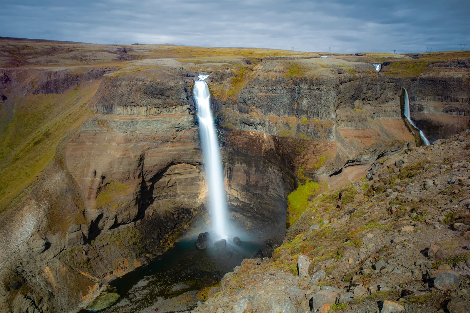 A single tall waterfall dropping into a banded rock canyon, the falling water blurred smooth by a long exposure.